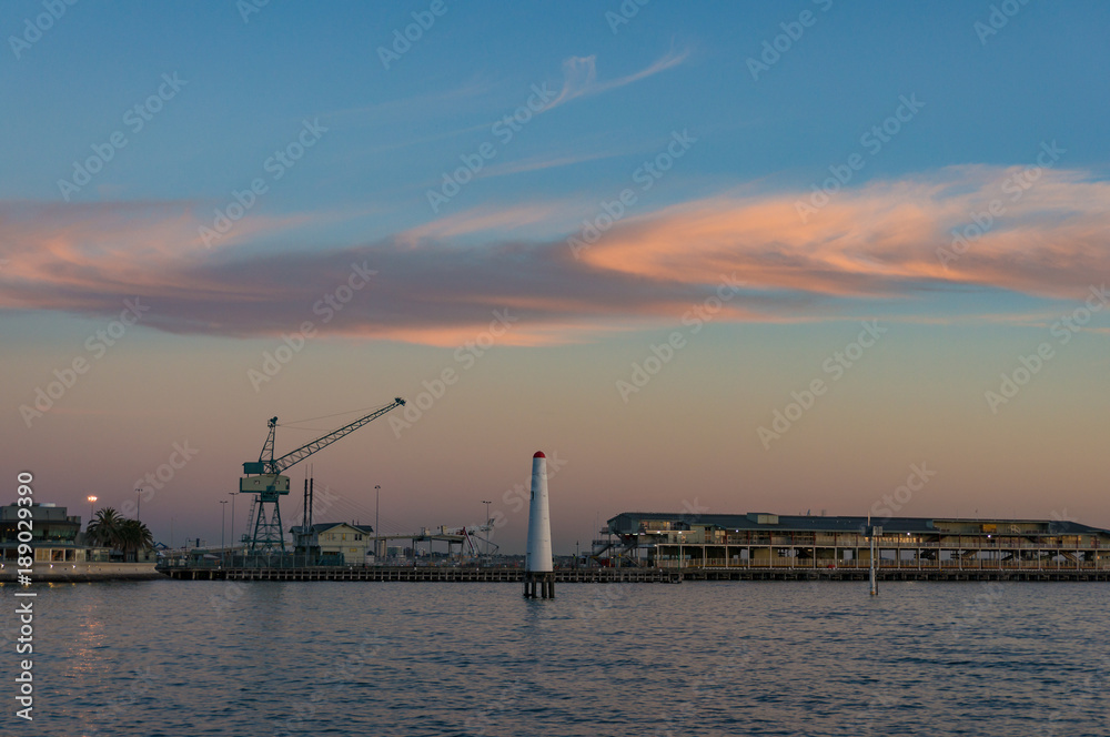 Wharf with hoisting crane and lighthouse at dusk