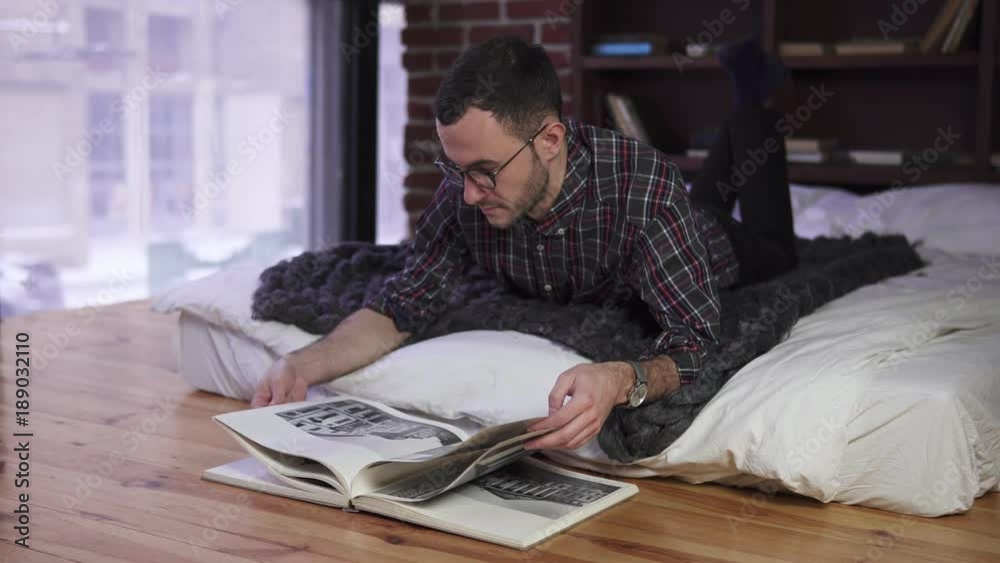 Young man with glasses reading a book on the bed Young man with glasses reading a book on the bed