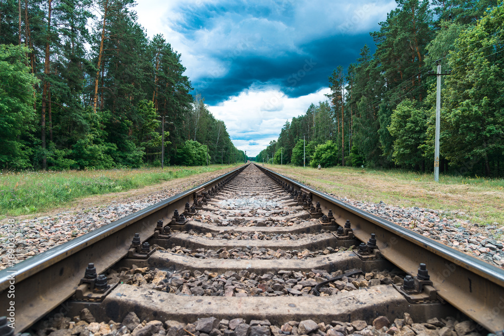Fototapeta premium Rusty railroad with rocks in the forest under dark blue cloudy sky
