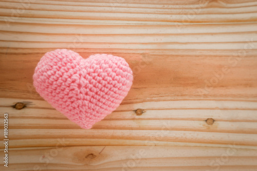 Pink heart knit with yarn on wooden floor.
