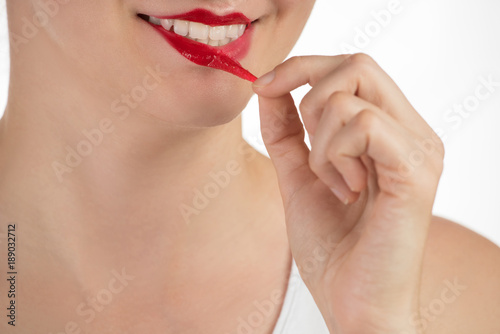 A beautiful girl applies a persistent liquid shiny red lipstick from a tube to her lips, and then takes it off as a film