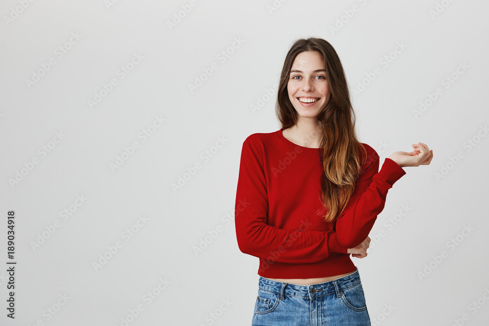 Close up studio portrait of young attractive caucasian female student with long hair in red jumper and denim jeans smiling with teeth, looking in camera with happy and satisfied face expression Close up studio portrait of young attractive caucasian female student with long hair in red jumper and denim jeans smiling with teeth, looking in camera with happy and satisfied face expression