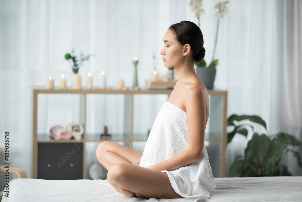 Side view profile of relaxed asian girl enjoying meditation in cozy atmosphere. She is sitting in lotus position at wellness center Side view profile of relaxed asian girl enjoying meditation in cozy atmosphere. She is sitting in lotus position at wellness center