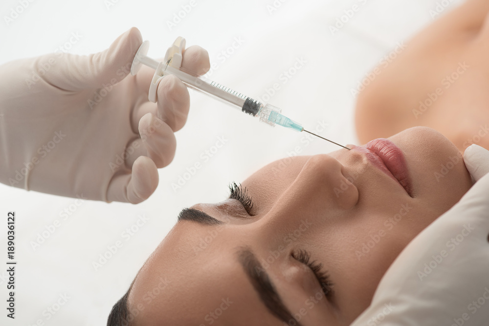Close up of surgeon arm holding syringe needle near female lips. Anti-aging procedure concept Close up of surgeon arm holding syringe needle near female lips. Anti-aging procedure concept