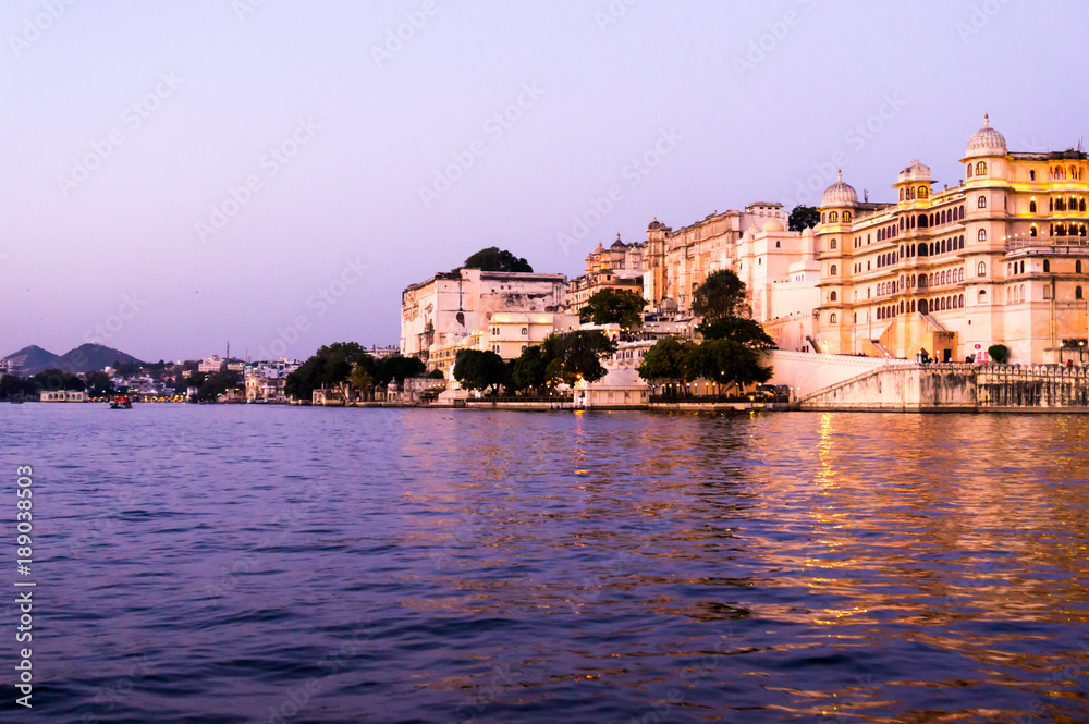 Udaipur city palace as seen from a boat on lake pichola at dusk with the purple gold tones. The sunset boat ride is a popular tourist activity