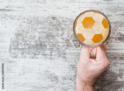 man s hand holds a beer mug with a football on a beer foam. Top view. Space for text