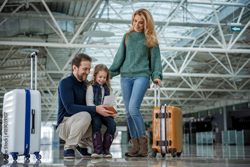 Full length of smiling family with suitcases going abroad. Father and daughter are looking at documents