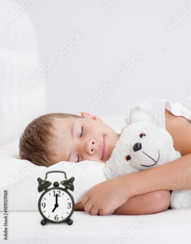 Happy little girl sleeping in bed with toy bear. Space for text
