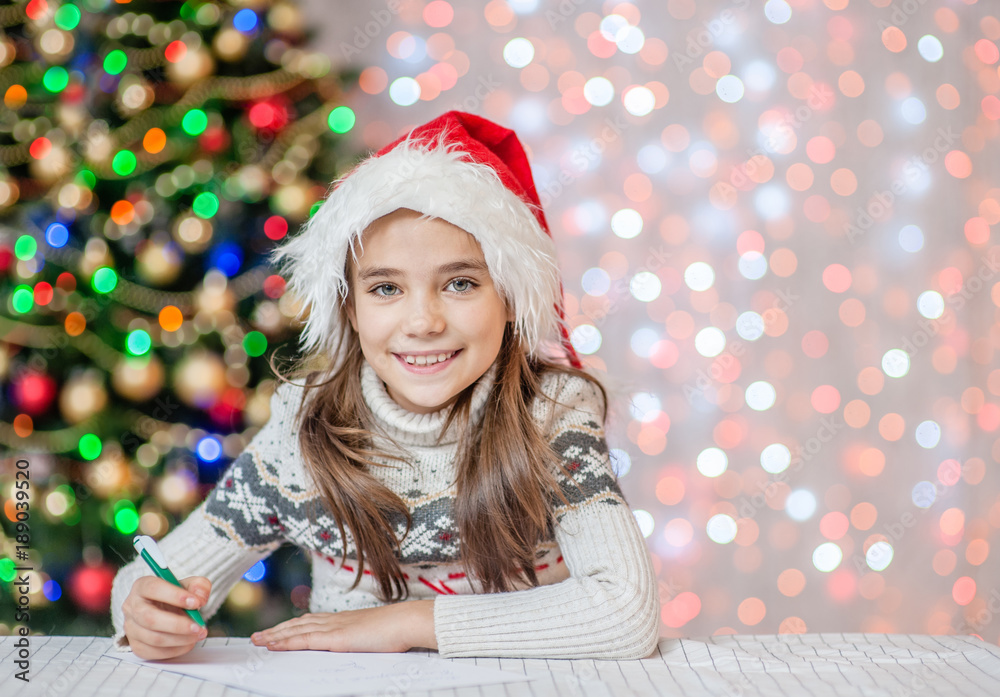 Happy little girl in red christmas hat writes letter to Santa Claus. Space for text Happy little girl in red christmas hat writes letter to Santa Claus. Space for text