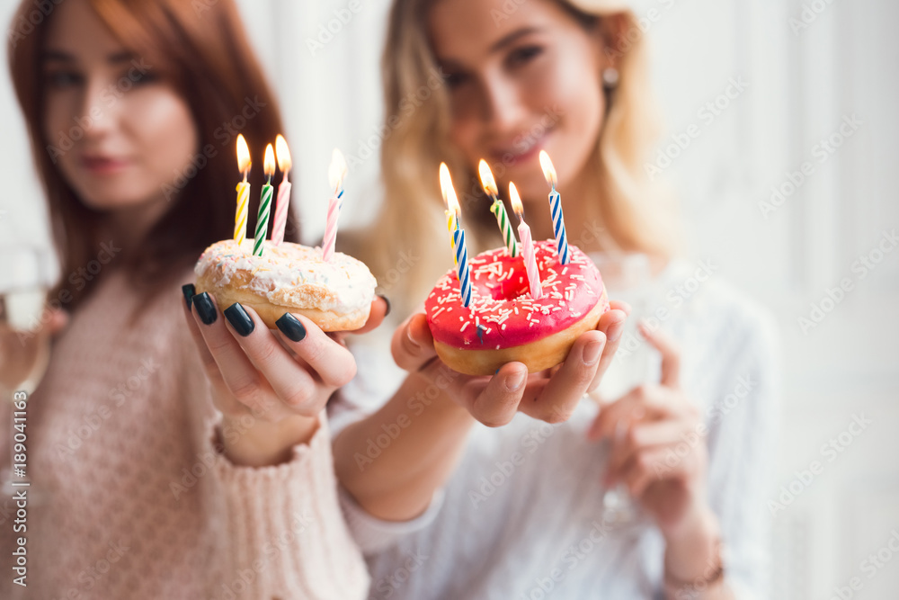 Two girls are holding and showing donuts.Birthday cakes. Celebration of the party. Holiday mood. Two girls are holding and showing donuts.Birthday cakes. Celebration of the party. Holiday mood.