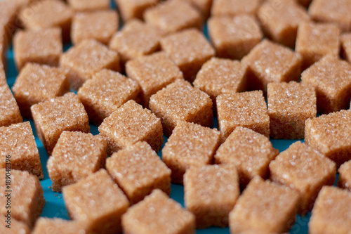 Brown cane sugar cubes scattered on a black background. Texture background