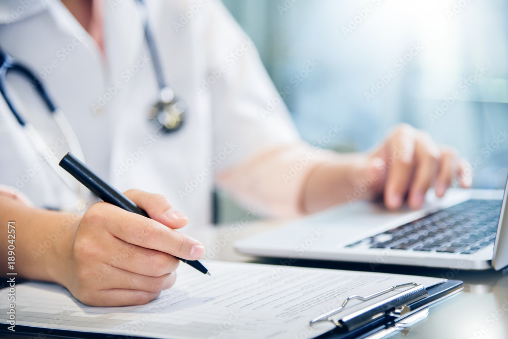 female doctor is using laptop and writing something on clipboard. female doctor is using laptop and writing something on clipboard.