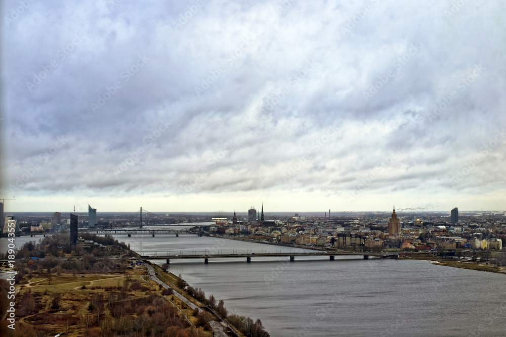 A view on city from television tower in Riga, Latvia. There are bridge, Dolgava river and buildings under the cloudy sky