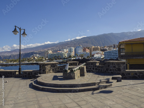 old copper cannons on paved sea front with lamp and view on  sea with big hotel resort buildings panorama of Puerto de la cruz  tenerife with green hill and blue sky background