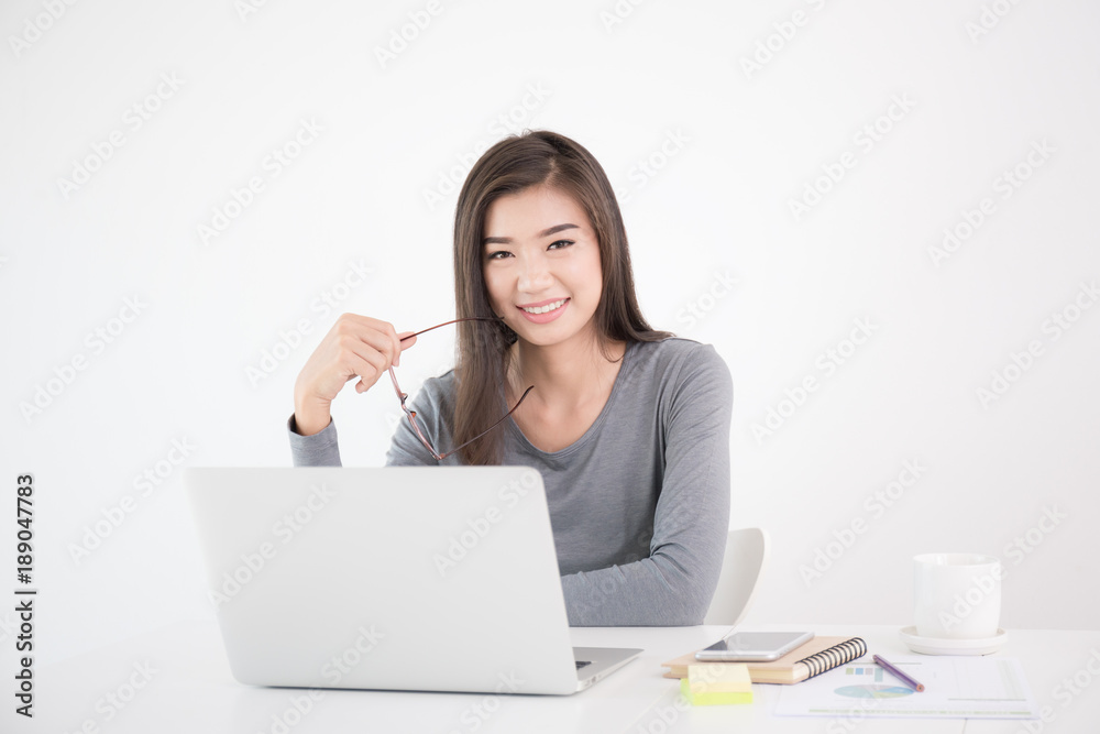 Asian woman holding glasses in hand and using laptop,Female smiling happily working in a white office desk Asian woman holding glasses in hand and using laptop,Female smiling happily working in a white office desk