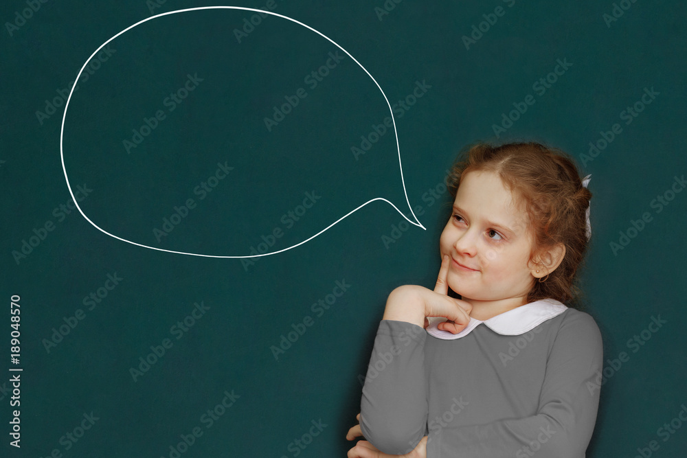 Smart curly girl near green chalkboard in classroom.