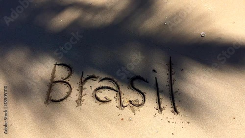 Brasil message handwritten on a smooth sand beach with palm tree shadows waving in the tropical wind
