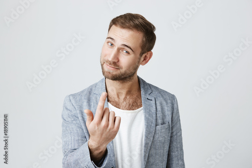Photography Handsome man with dark hair, stylish haircut, blue eyes, and beard looks with appeal at camera, isolated against gray background