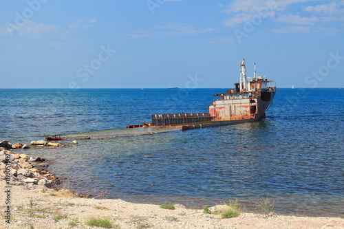 Unknown semi-submerged rusted and destroyed barge stranded in a bay