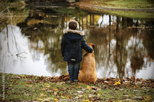 Kleiner Junge mit Hund steht am Ufer eines Sees und schaut auf Wasser