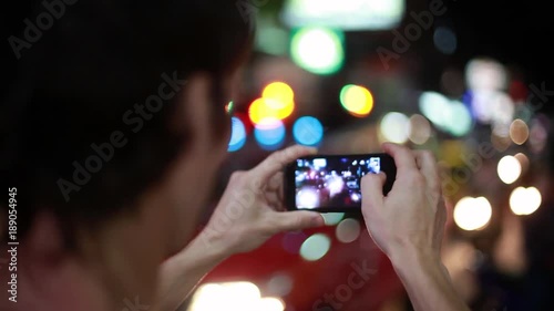 Close up of tourist with mobile phone takes picture in the night street with bokeh lights. 1920x1080