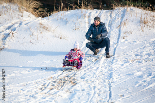 Little girl child is towing with the sledge by gradfather in park in winter photo