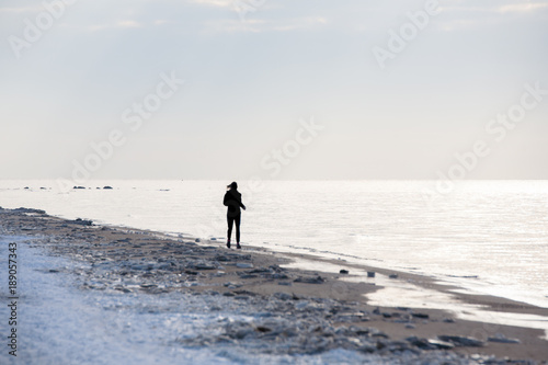 silhouette young fit woman is jogging running on a snow on the beach in winter. Sport and fitness
