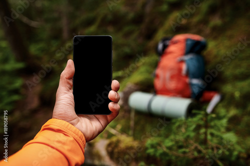 Hand of young man, which is standing on the rock and holding smart phone