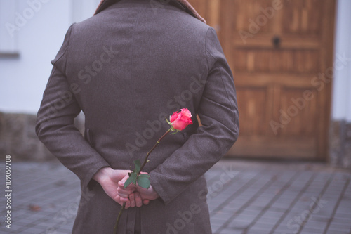 Man holding rose hiding on back at the park. Womans / Valentines Day concept.