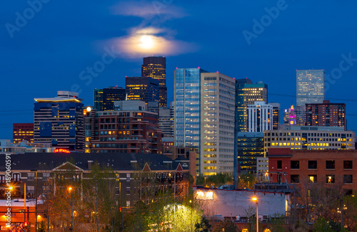 Colorful lights of the Denver Colorado downtown skyline at night with the full moon glowing in the evening sky in the background