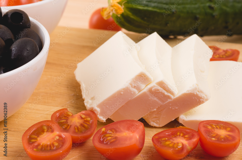 Greek salad with vegetables, feta cheese, black olives in process. Wooden background . Top view Greek salad with vegetables, feta cheese, black olives in process. Wooden background . Top view