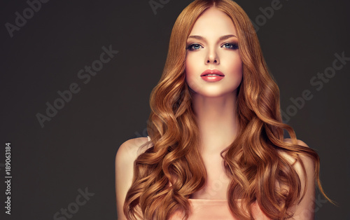 Fototapeta Czerwona głowa dziewczyna o długich i lśniących falowanych włosach. Piękna wzorcowa kobieta z kędzierzawą fryzurą.