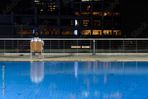 Asian's man sitting on Wooden chairs are located at the hotel's swimming pool at night. © Vatcharachai