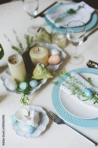easter and spring festive table decorated in blue and white tones in natural rustic style, with eggs, bunny, fresh flowers and candles.