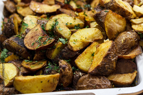 Freshly fried potato wedges with herbs and garlic on a baking sheet