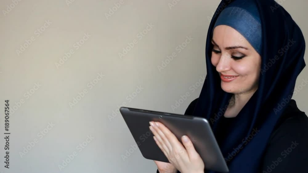 Portrait of a beautiful Arab woman who smiles and looks at the screen of a tablet and dials a message, communicates on the Internet and social networks, using a Tablet PC. Lifestyle and leisure of Portrait of a beautiful Arab woman who smiles and looks at the screen of a tablet and dials a message, communicates on the Internet and social networks, using a Tablet PC. Lifestyle and leisure of