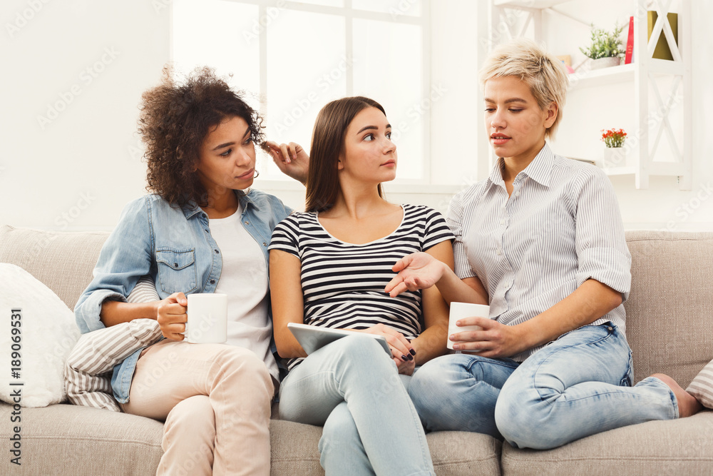 Three female friends using tablet and drinking coffee