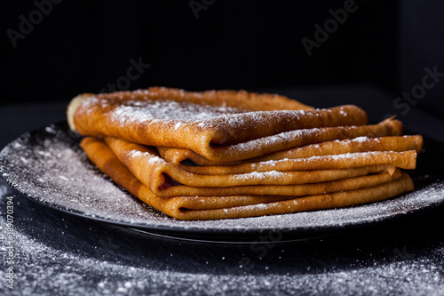 Stack of crepes with powdered sugar on dark background. Maslenitsa. Russian folk festival