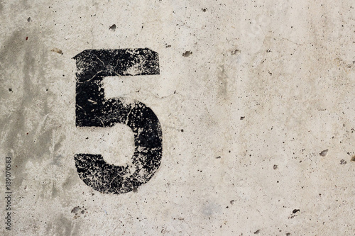 Number 5 five black sign on concrete wall closeup with copyspace photo