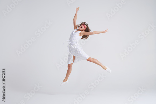 Young charming female in dress jumping over white background