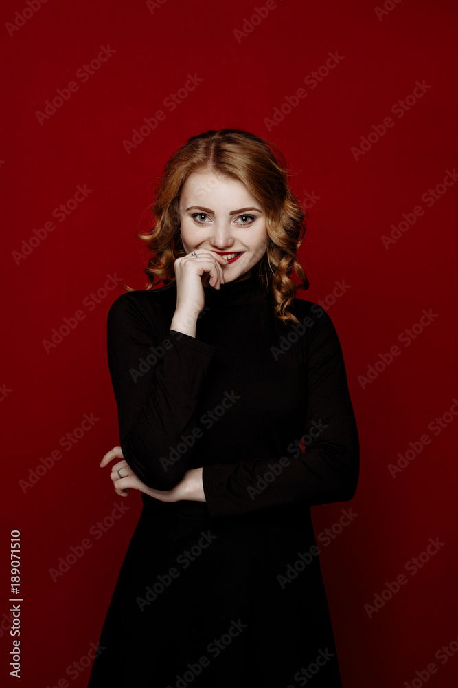 young stylish blond girl in black clothes posing in the studio isolated on red background. woman rejoices smiles and looks in the camera young stylish blond girl in black clothes posing in the studio isolated on red background. woman rejoices smiles and looks in the camera