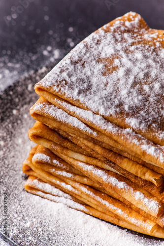 Stack of crepes with powdered sugar on dark background. Maslenitsa. Russian folk festival
