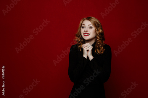 young stylish blond girl in black clothes posing in the studio isolated on red background. woman rejoices smiles and looks in the camera