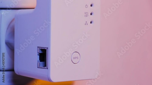 Man press with his finger on WPS button on WiFi repeater which is in electrical socket on the wall