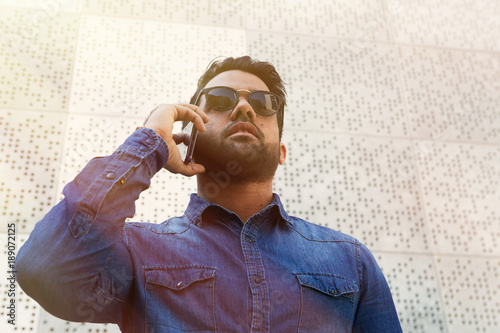 Attractive young man with cell phone outdoors making mobile call, successful confident hipster photo