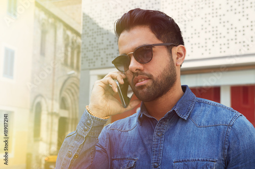 Attractive young man with cell smiling guy relaxing outdoors making mobile call, successful confident hipster having pleasant phone conversation. photo