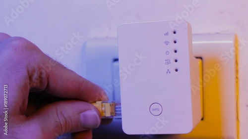 Man insert ethernet cable into WiFi extender device which is in electrical socket on the wall