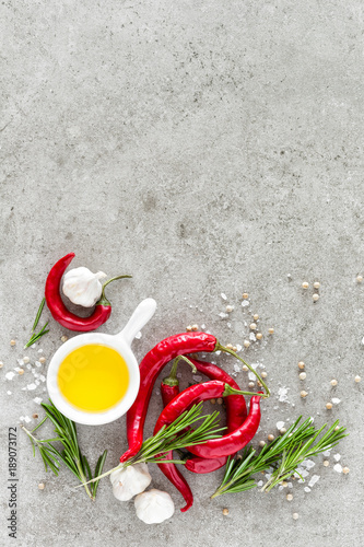 Culinary background with a space for a text, flat lay composition of oil, chili peppers, rosemary, garlic and spices on a table stone surface, top view