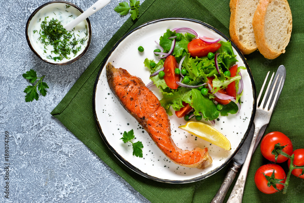 Food background. Baked trout with garnish of vegetable salad and avocado, with cream sauce on a concrete background.