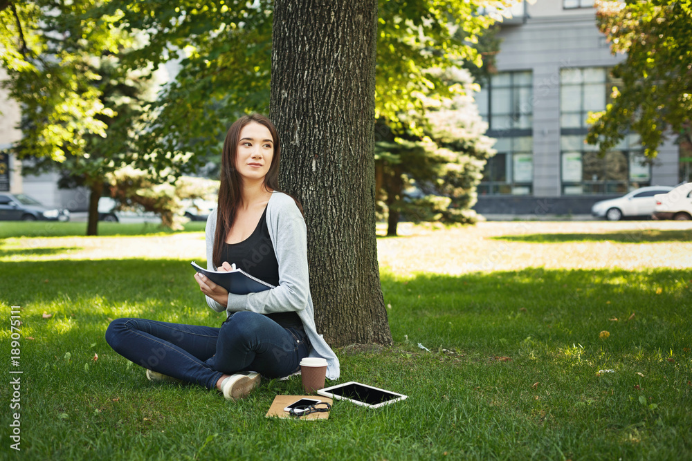 Young woman sitting with notebook on grass Young woman sitting with notebook on grass